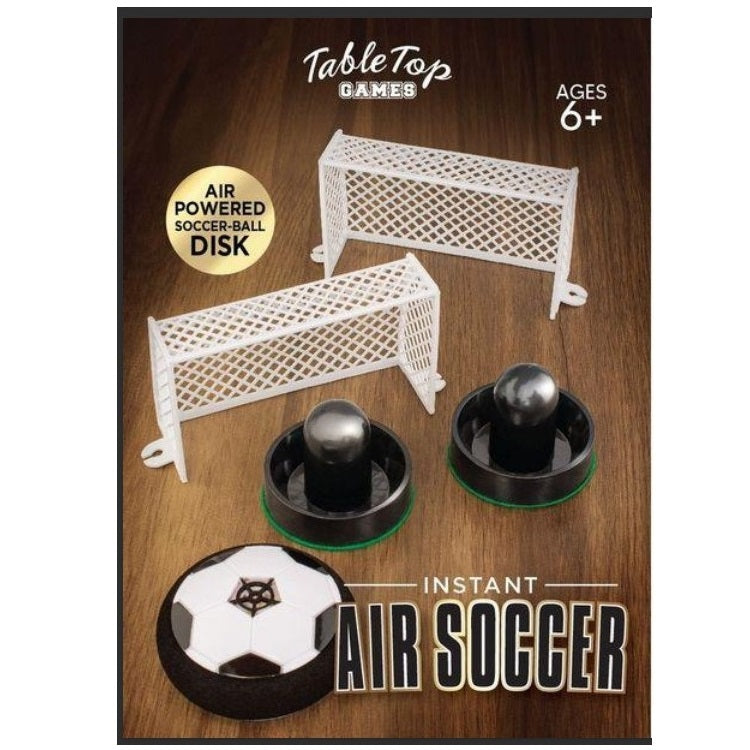 Product packaging for an "Instant Air Soccer" game featuring two white soccer goals, two pucks, and a disc-shaped air-powered soccer ball. The packaging also displays the brand "TableTop Games" and an age recommendation of 6+. The game is showcased on a wooden surface.