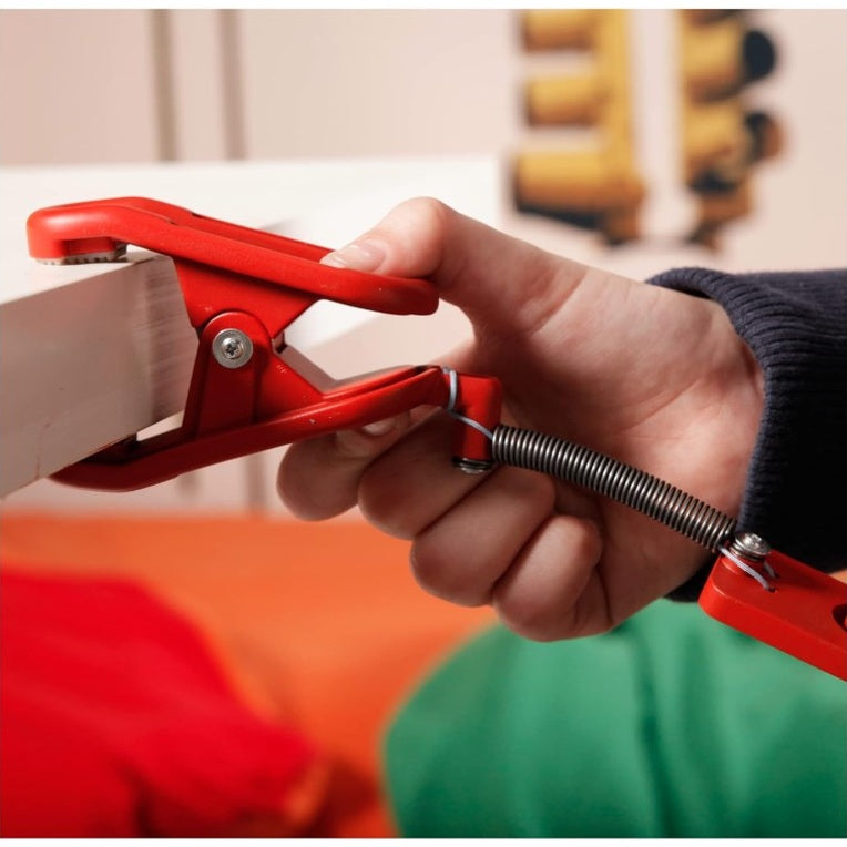 A person's hand holds a red spring clamp onto a white object.