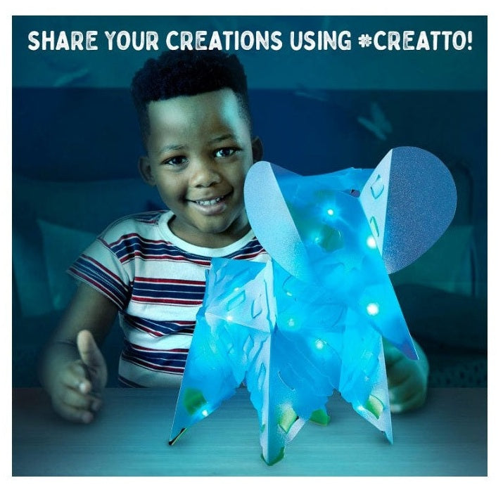 A child displays a blue, lighted Creatto creation on a table.