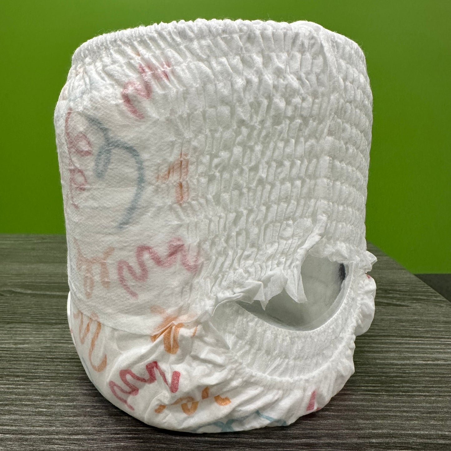 White diaper pants with colorful designs, displayed on a wood-grain surface.