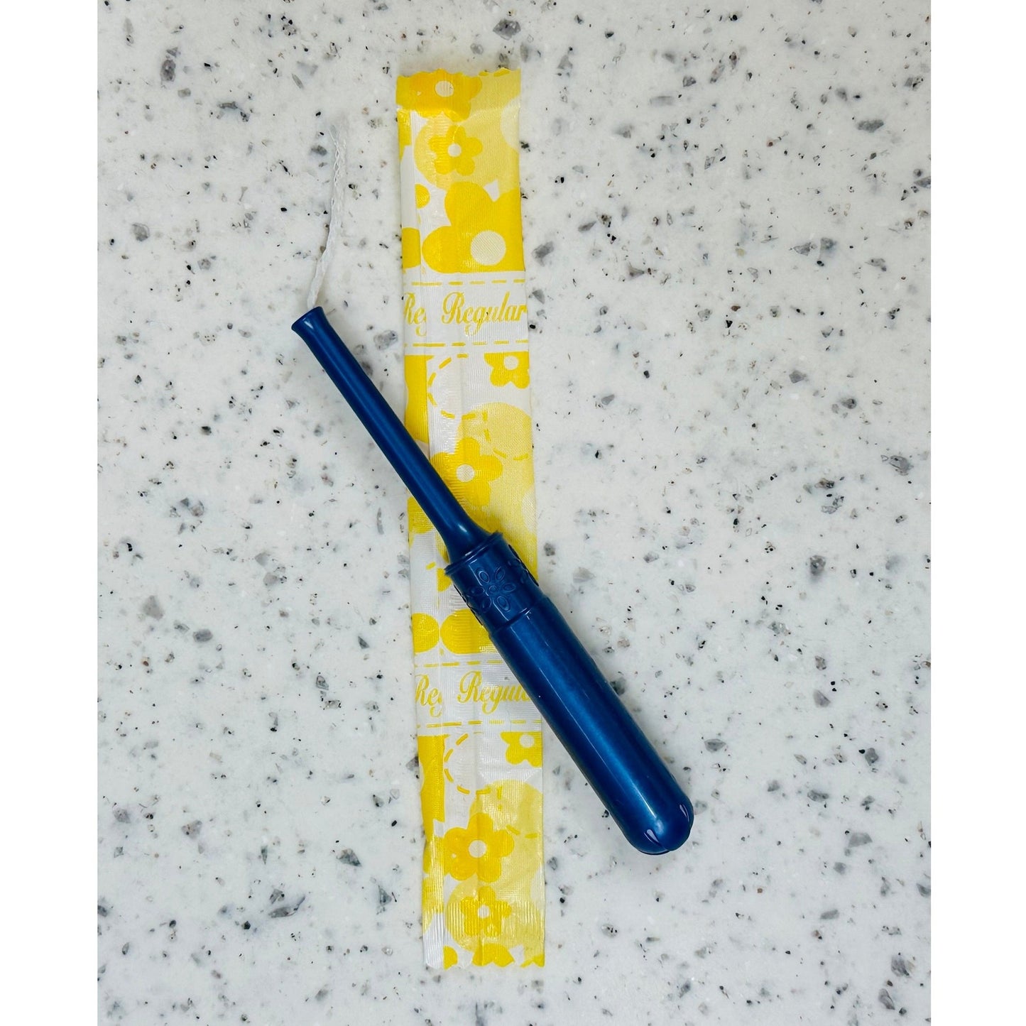 Blue tampon applicator over a yellow and white tampon wrapper on a countertop.
