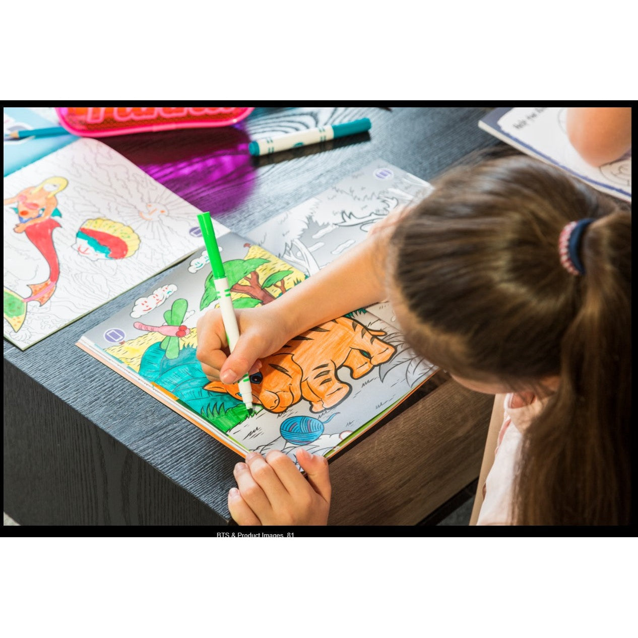 A girl coloring a tiger in a coloring book with a green marker.