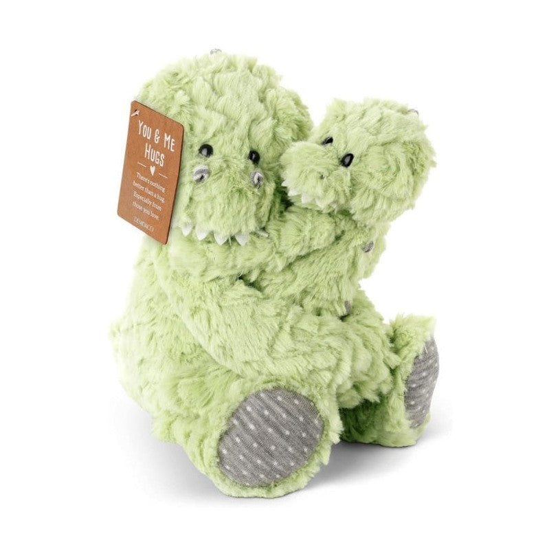 Two light green fuzzy dinosaur stuffed animals hugging each other with a brown tag that reads "YOU & ME HUGS".