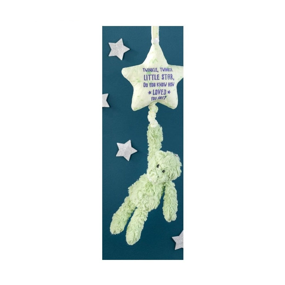 A hanging baby mobile toy with a plush green bear dangling from a plush yellow star against a dark blue background with silver stars.