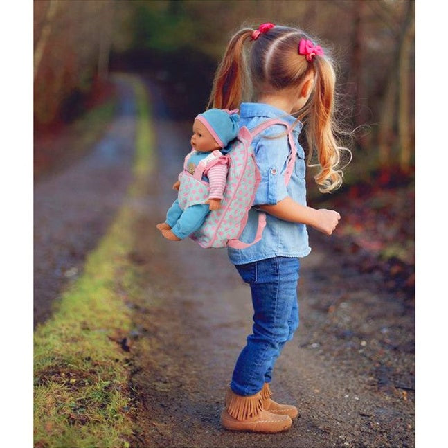Young girl in jeans, denim shirt, and moccasins carries a doll in a pink baby carrier backpack.