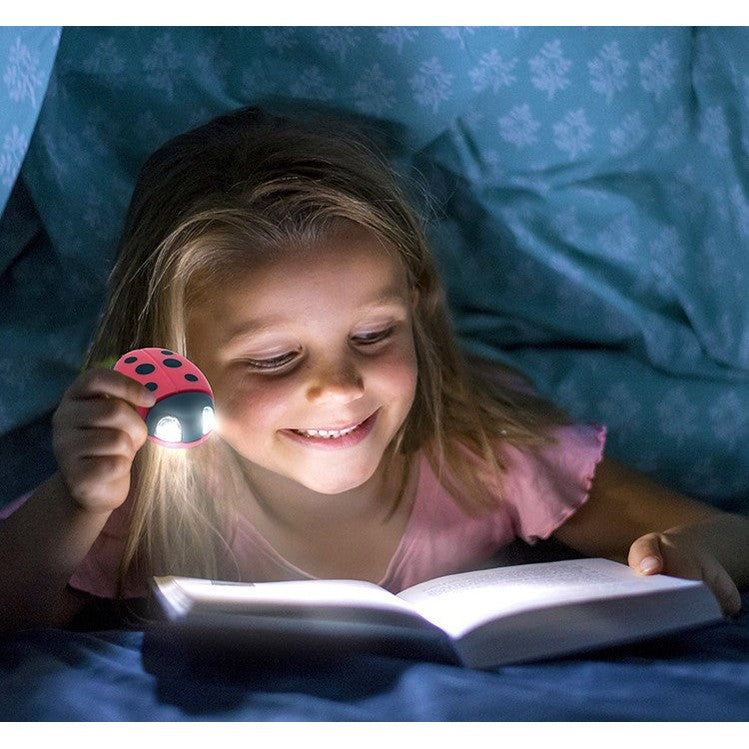 Girl reading a book in bed with a ladybug-shaped flashlight.