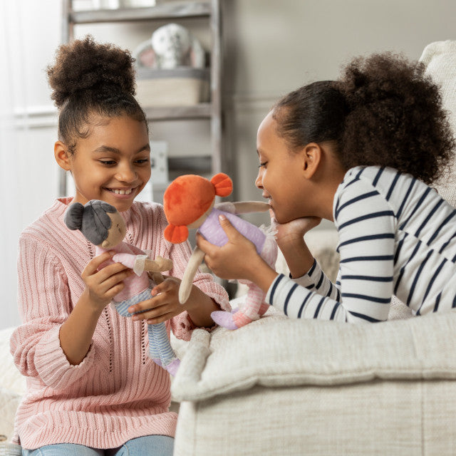 Two young girls playing with dolls indoors.