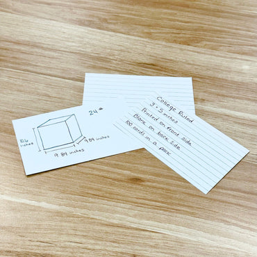 Three index cards with handwritten text and a drawing on a wood surface.