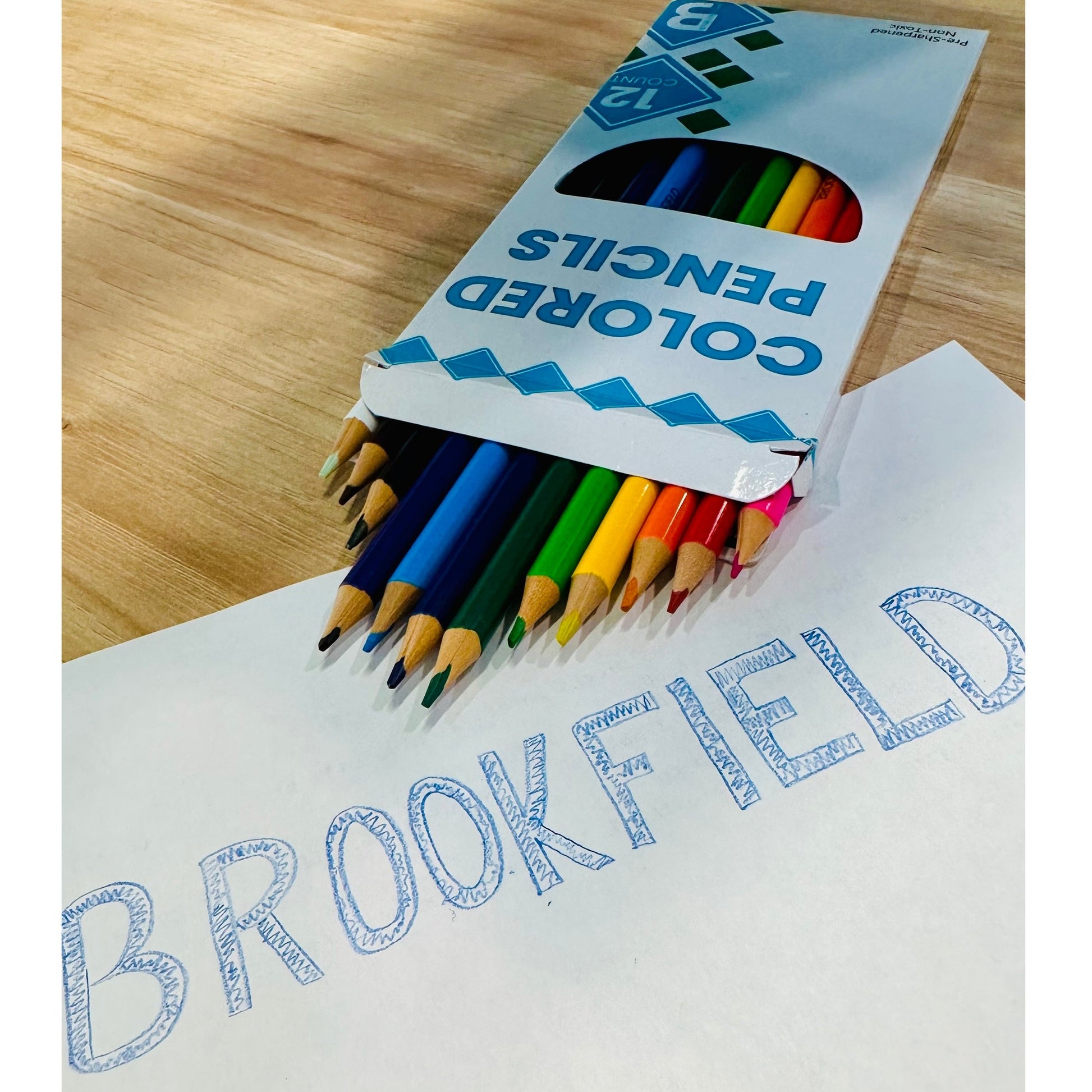 Colored pencils in a box next to the word "BROOKFIELD" written on white paper.