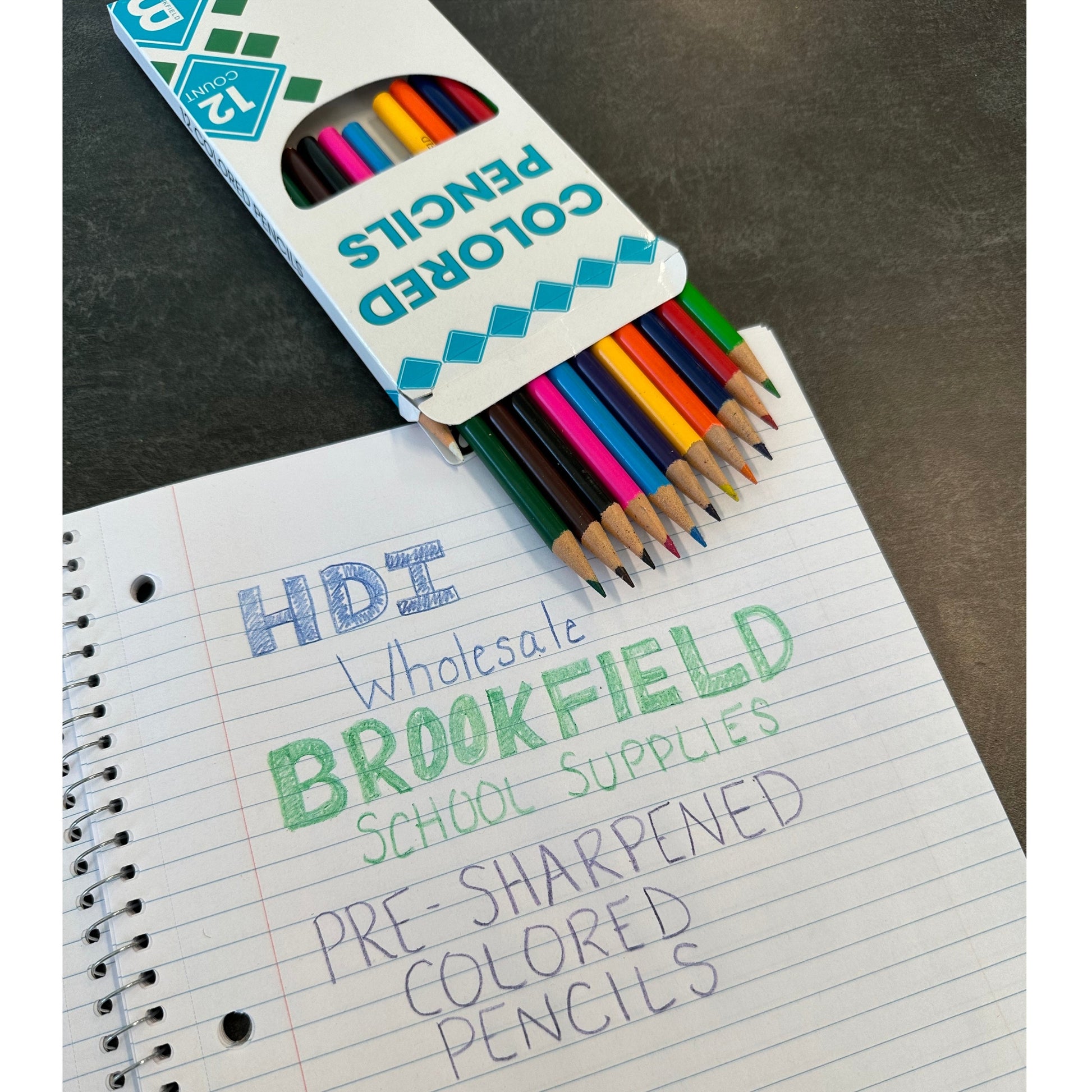 Open box of 12 count pre-sharpened colored pencils on a lined notebook with handwritten words.