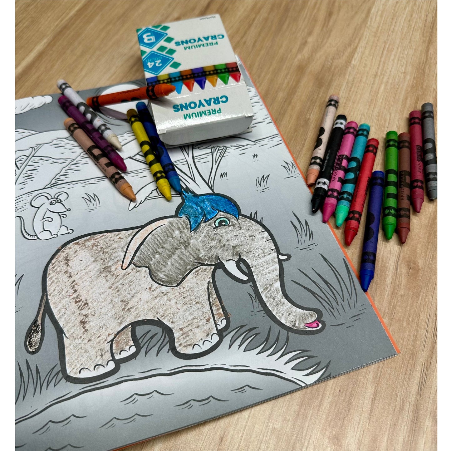 A coloring book with an elephant, crayons, and a crayon box on a wooden surface.