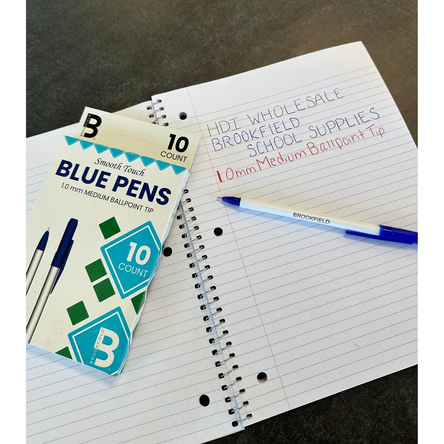 Image shows a pack of blue ballpoint pens next to a notebook with some text written on it.