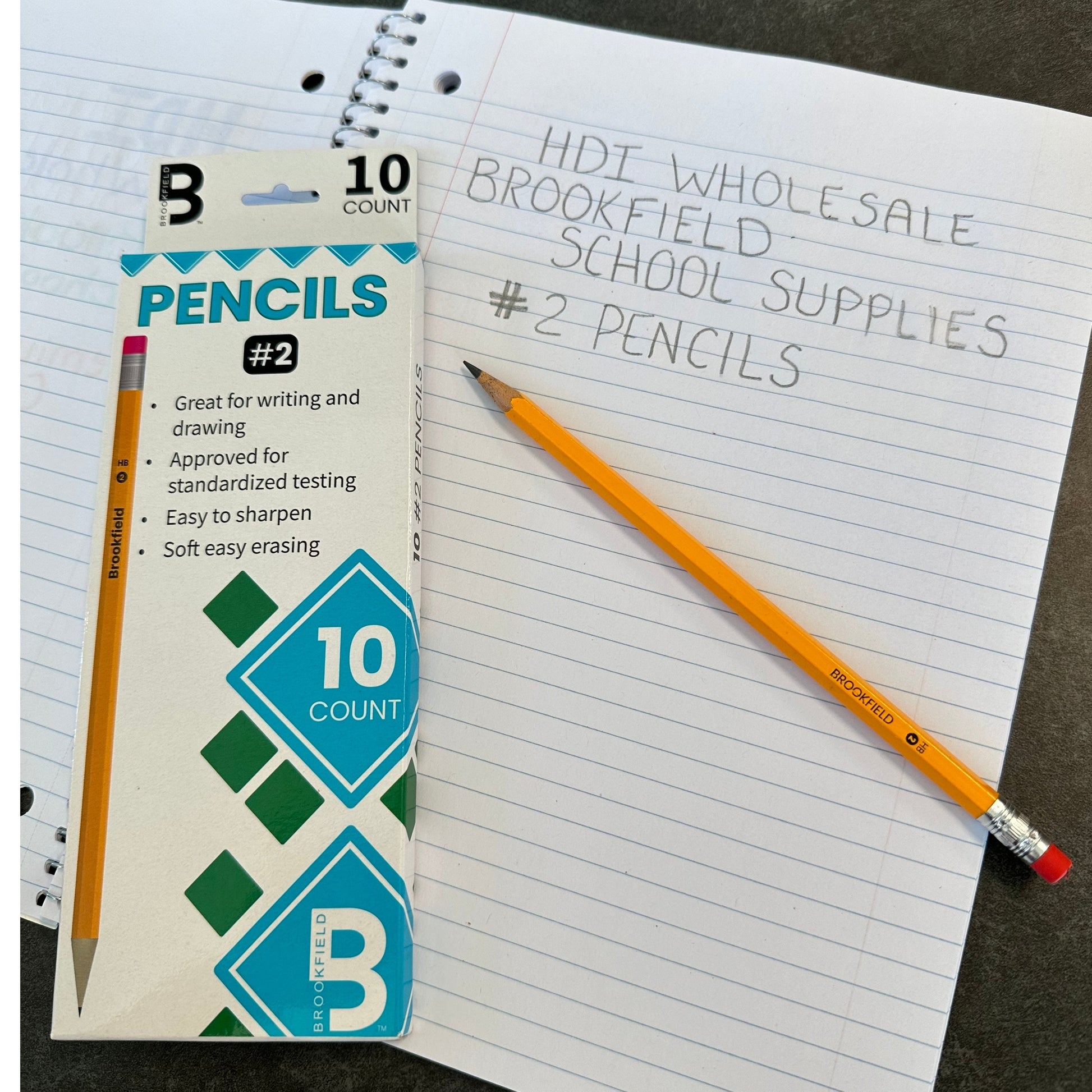 Overhead shot of a box of Brookfield #2 pencils next to a sharpened yellow pencil and a notebook with handwritten words on the lined pages.