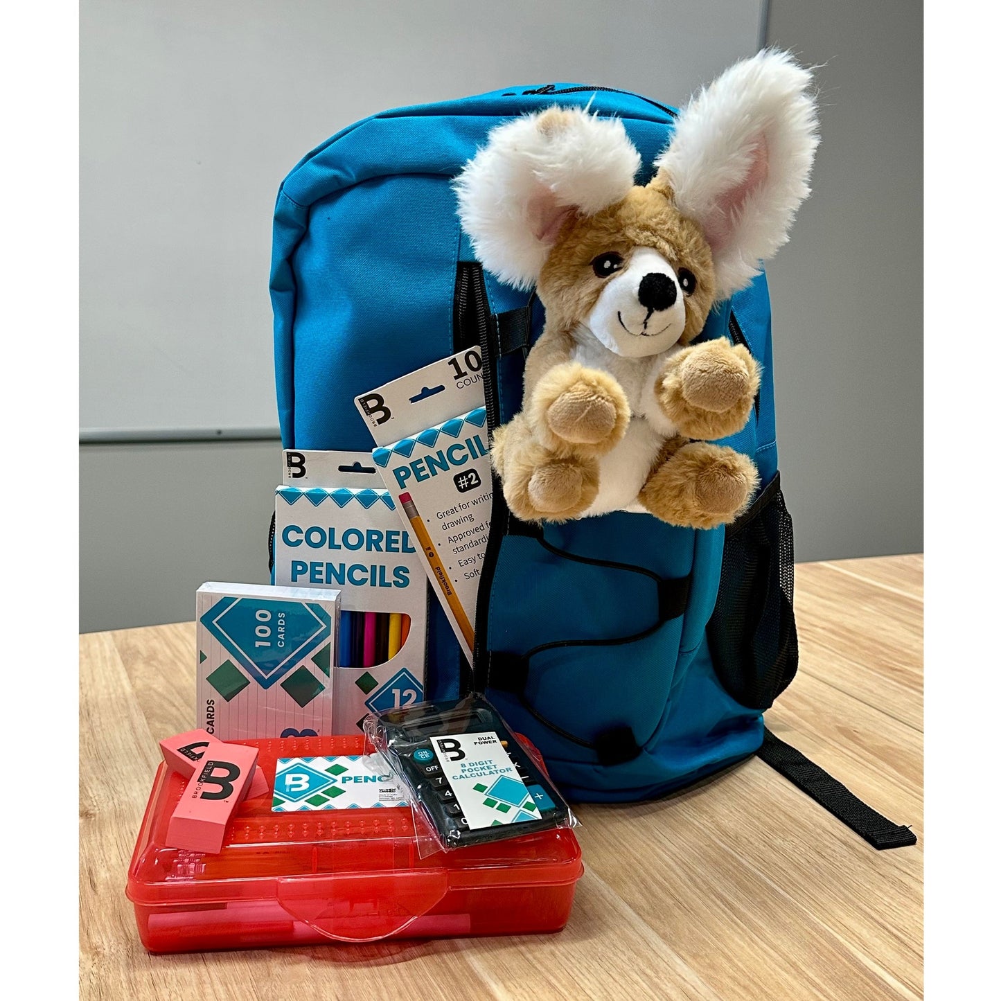 A blue backpack with school supplies and a stuffed animal on a wooden table.