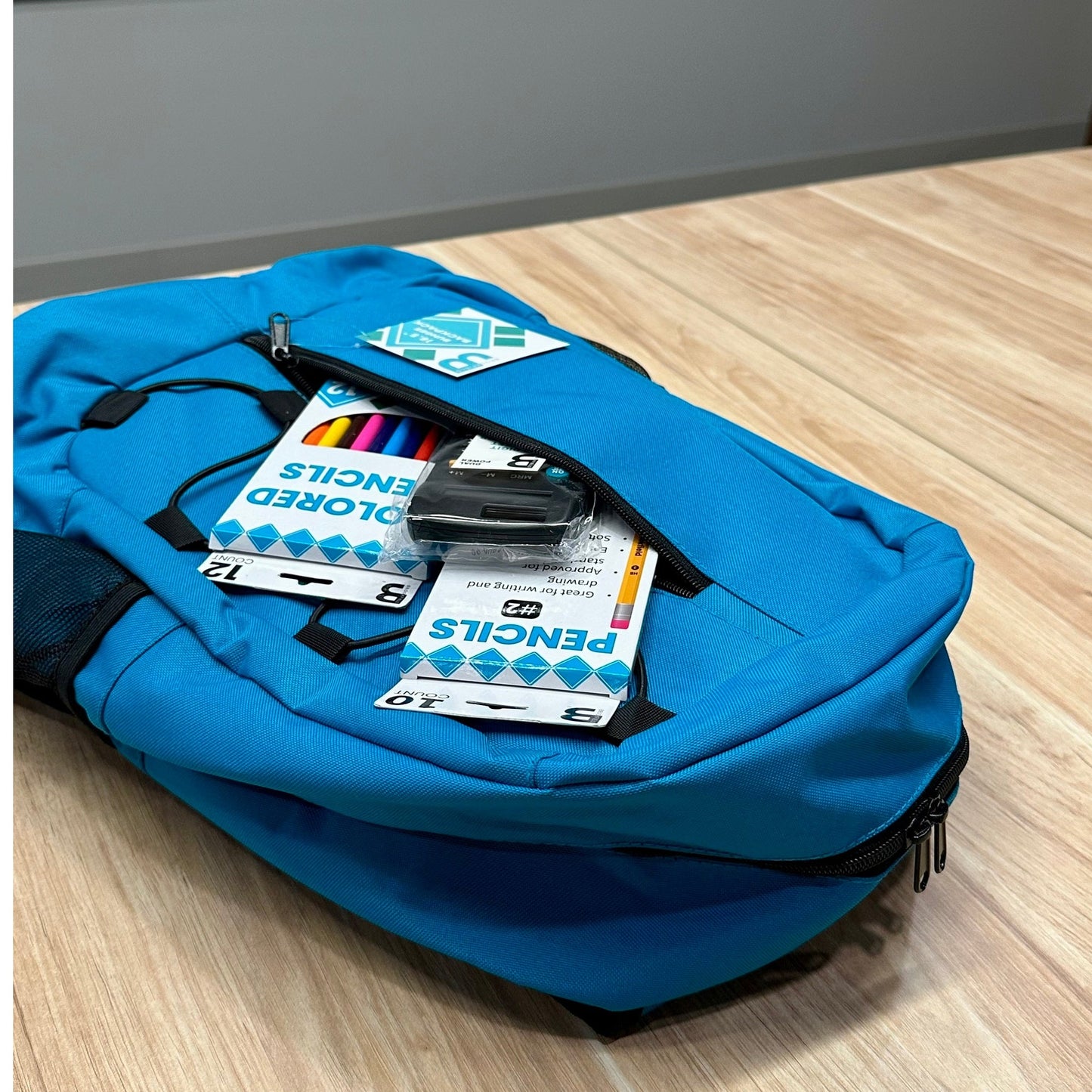 Close-up of a blue backpack on a wood floor with pencils and a calculator in the front pocket.