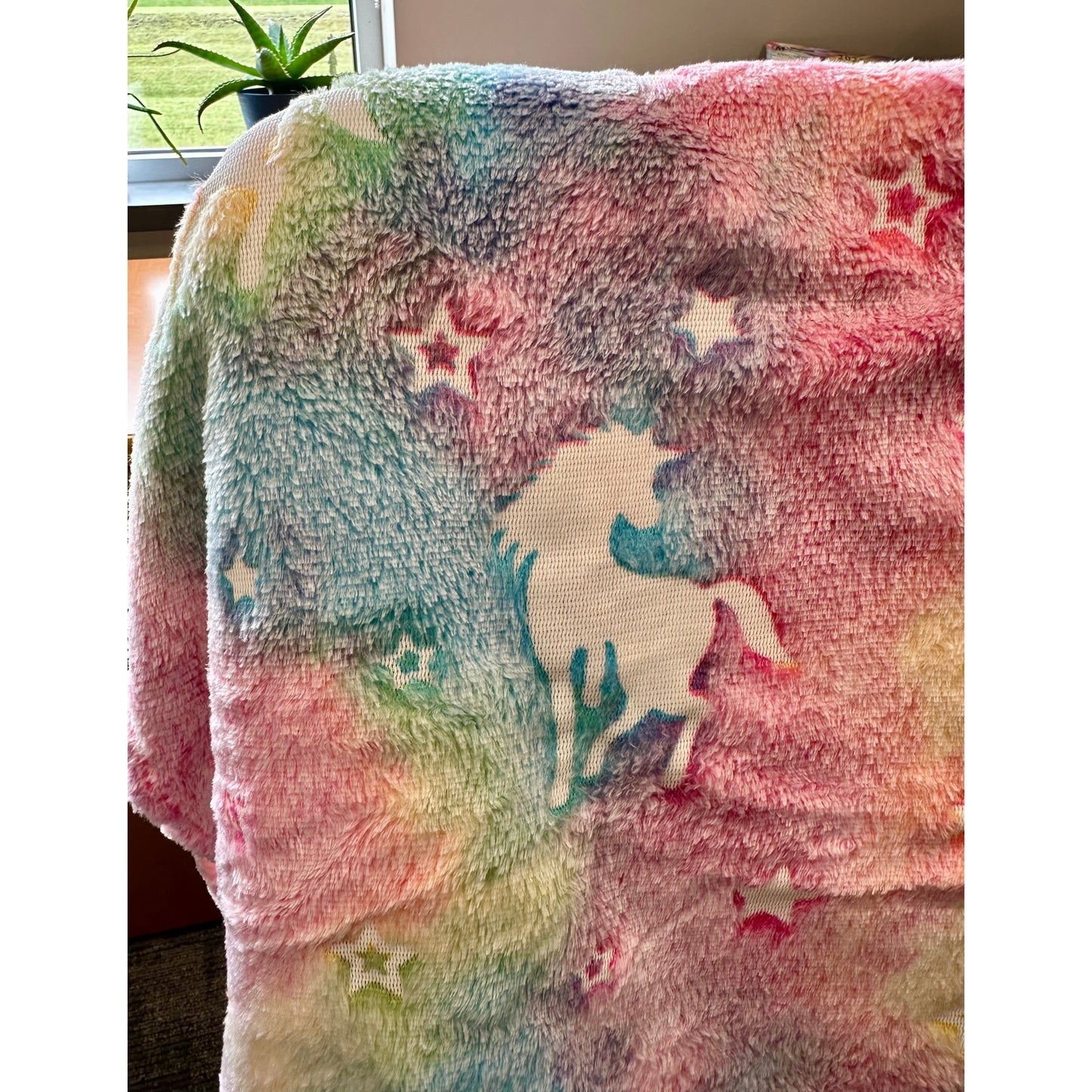Fuzzy rainbow-colored blanket with a unicorn and stars.
