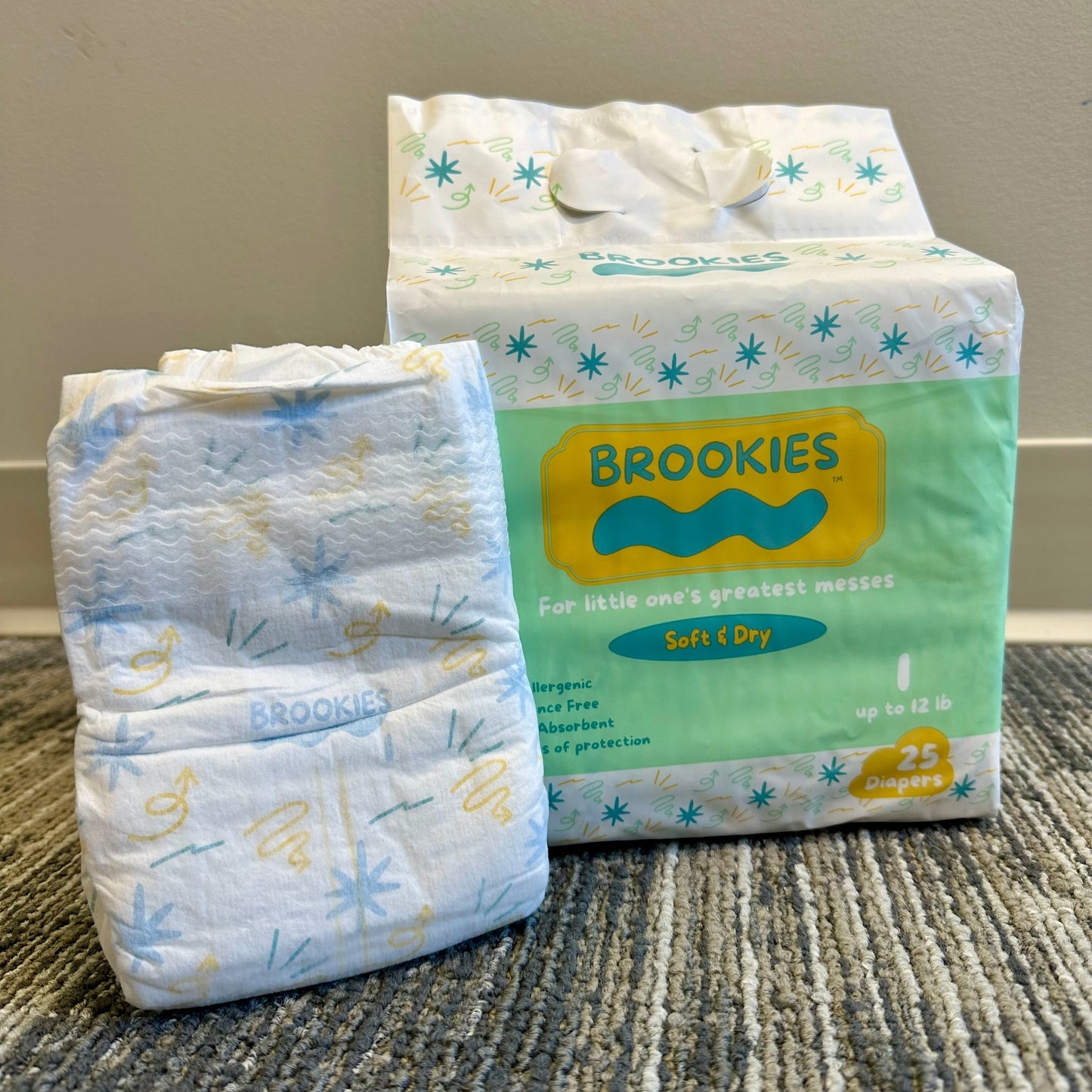 A package of "Brookies" diapers next to a single unfolded diaper, with a white background and a light-colored carpet.