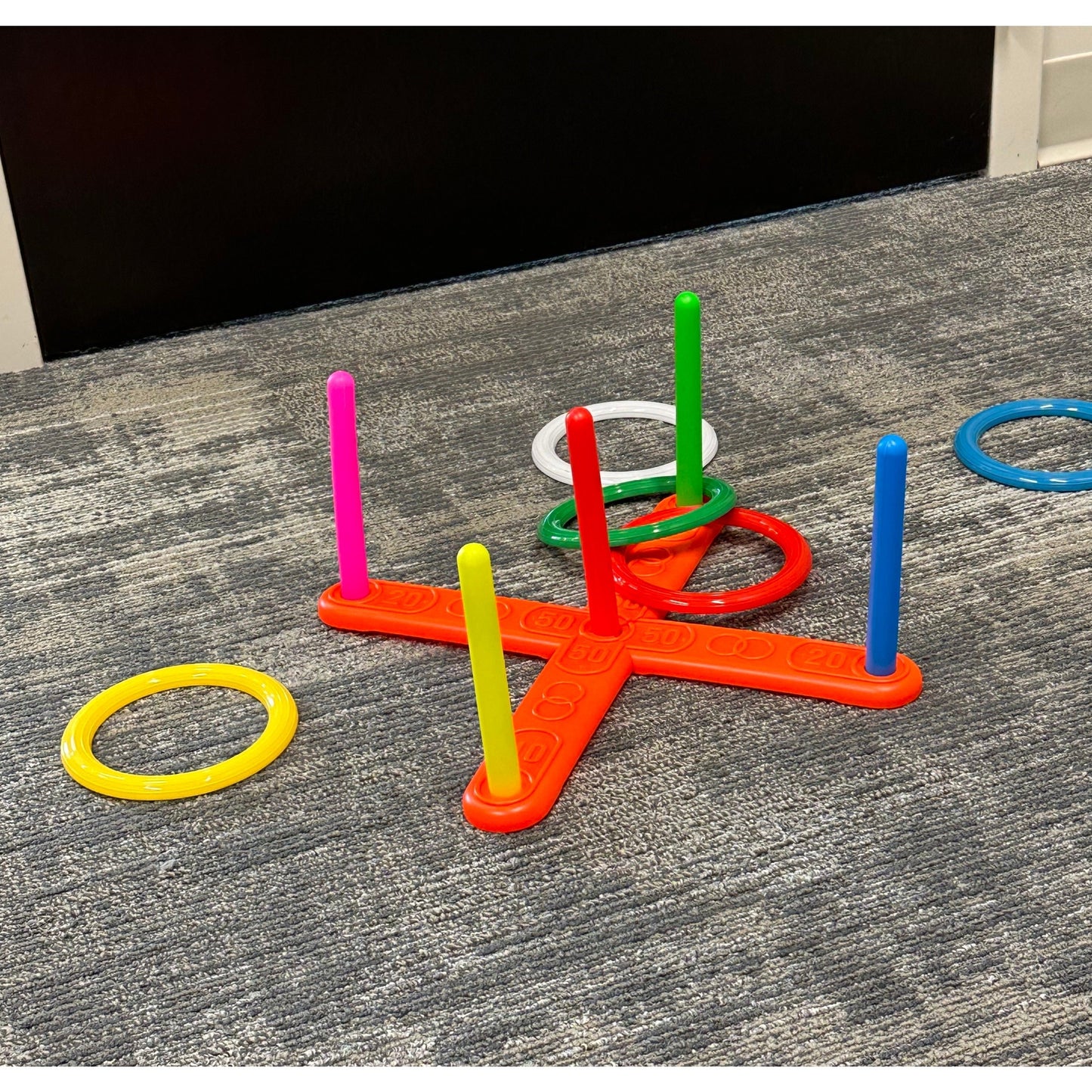 A ring toss game with a brightly colored base and rings on a gray carpet.
