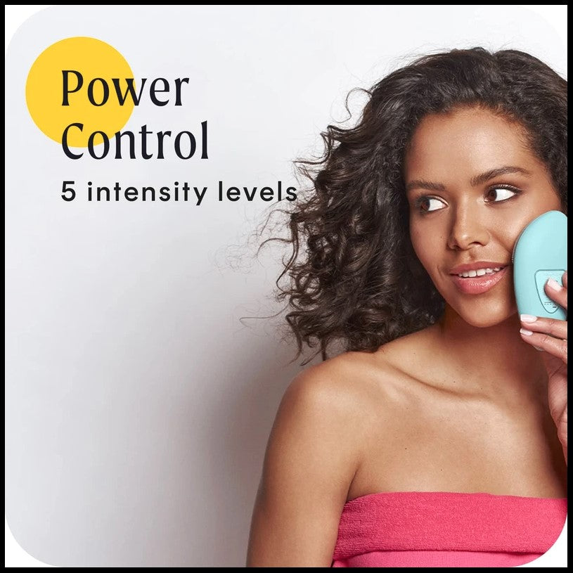 Woman wearing a pink towel holding a blue facial cleansing device.
