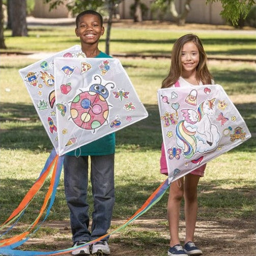 A boy and girl pose outdoors with kites.
