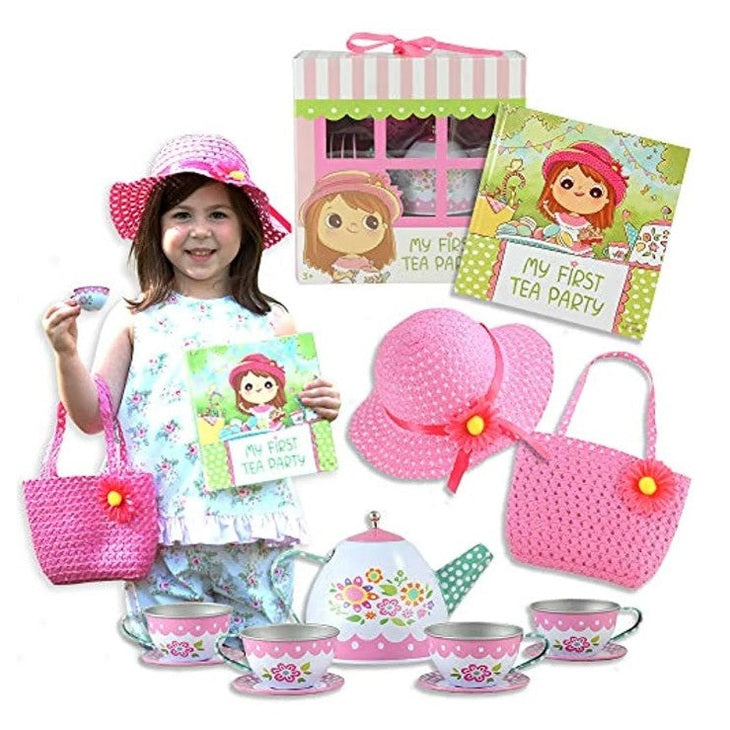 A girl wearing a floral outfit and pink hat, holding a tea set, book, and purse.