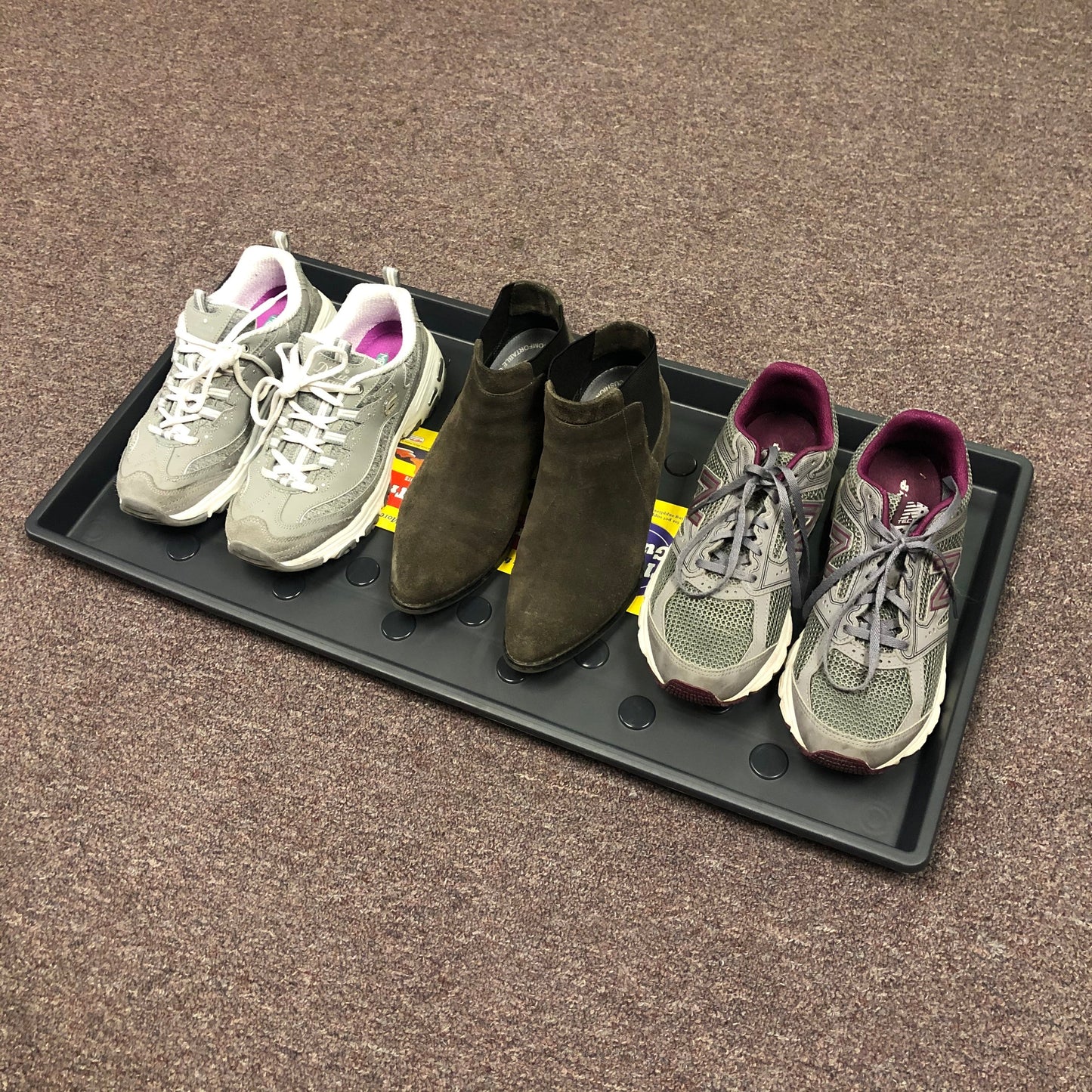 Three pairs of shoes on a black tray. Gray and white sneakers with pink trim, brown suede ankle boots, gray and purple New Balance sneakers.