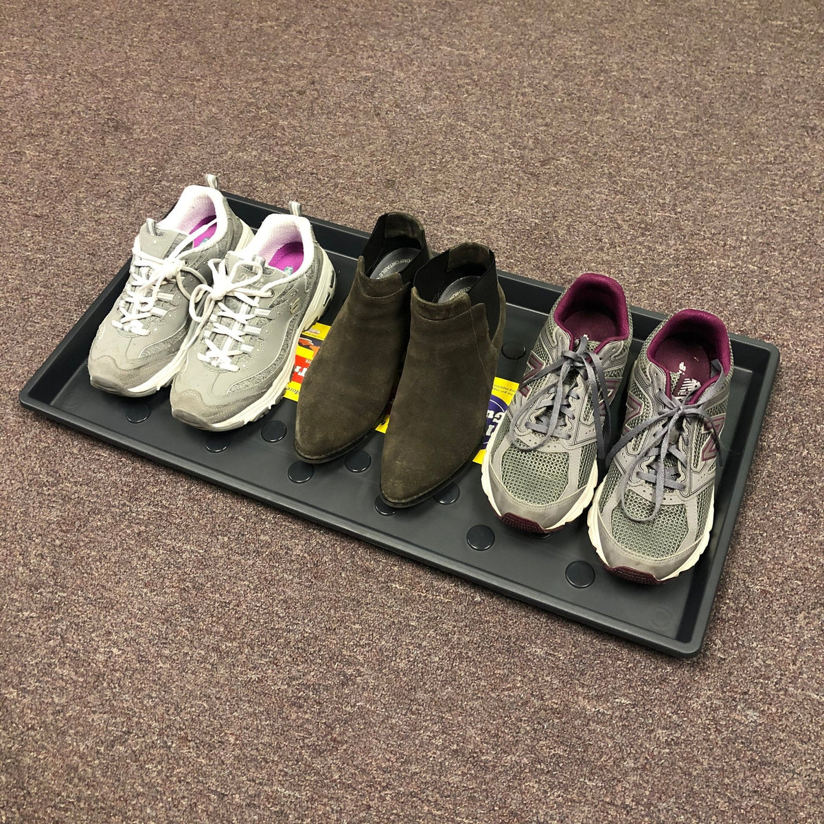 Three pairs of shoes on a black tray. Gray and white sneakers with pink trim, brown suede ankle boots, gray and purple New Balance sneakers.