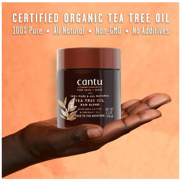 Close-up of a Cantu Tea Tree Oil jar held in a dark-skinned hand against an orange background.