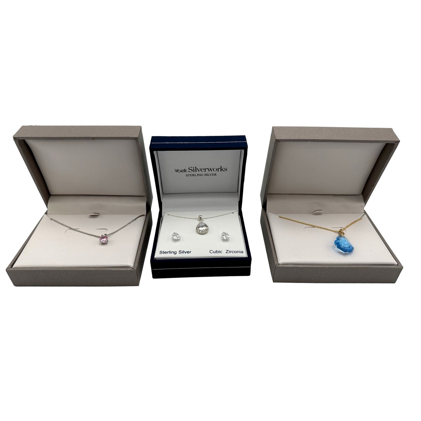 Three jewelry sets in open boxes. A pink necklace, a silver necklace and earring set, and a blue necklace.