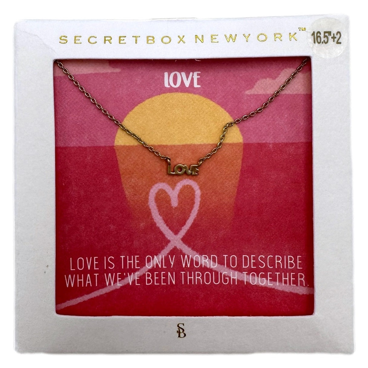 Gold-toned "love" pendant necklace with pink and yellow sunset-themed card in white frame.