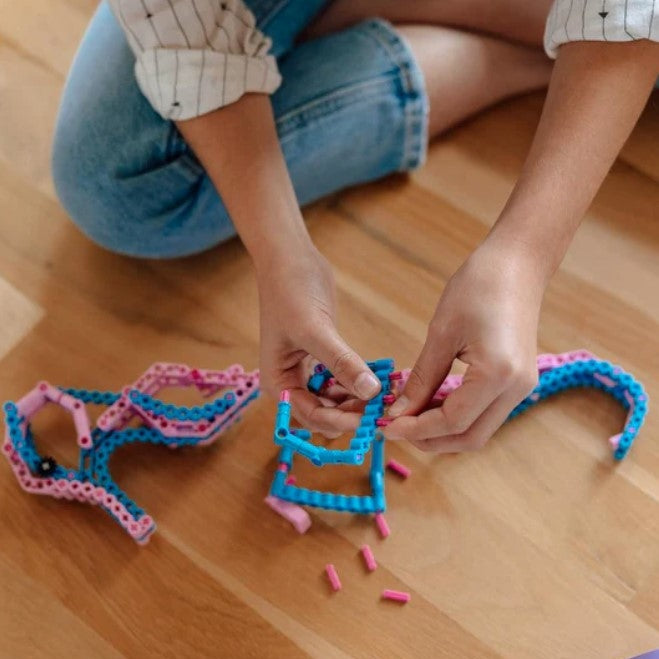 Person sitting on wood floor, building blue and pink toy.
