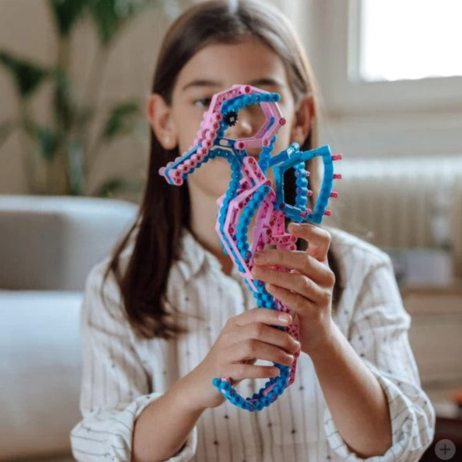 Girl holding a pink and blue building-block seahorse.