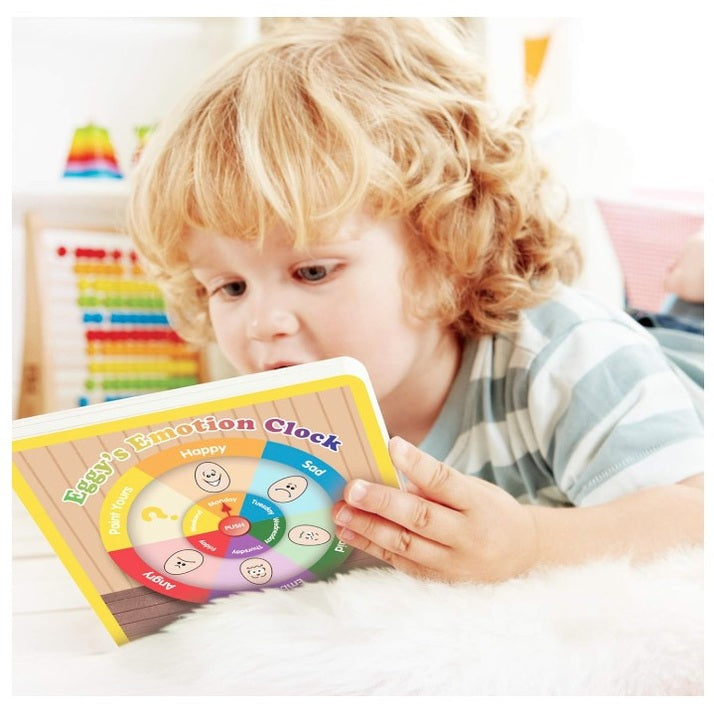 Child in striped shirt reads "Eggy's Emotion Clock" book while lying on white fur rug.