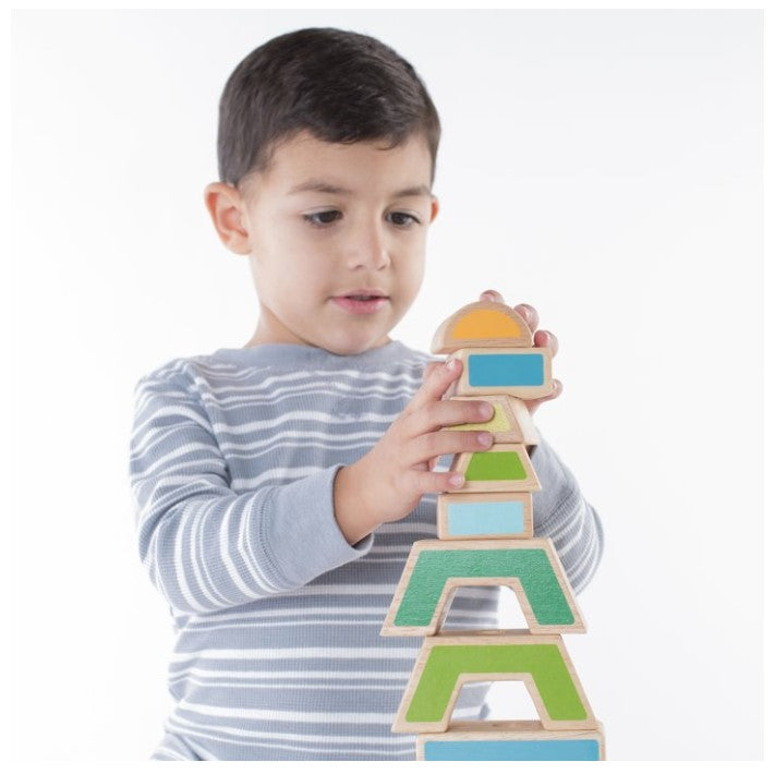 A young boy stacking colorful geometric blocks. He is wearing a striped shirt.