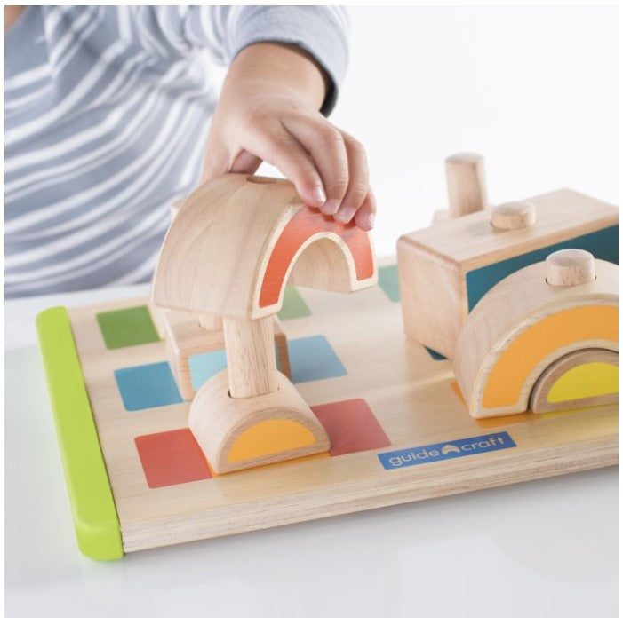 A child in a striped shirt playing with wooden building blocks on a colorful base.