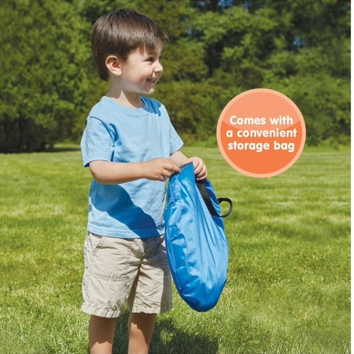 Child holding a blue storage bag outdoors with greenery in the background