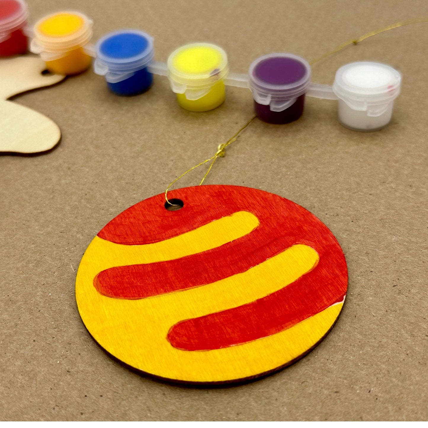 A painted wooden ornament with red and yellow stripes rests near a set of small paint containers.