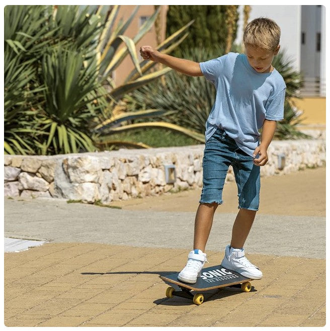 Boy on skateboard, wearing blue t-shirt, jean shorts, and white sneakers.
