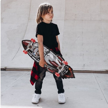 Young boy with skateboard wearing black t-shirt, jeans, white sneakers, and red plaid shirt.