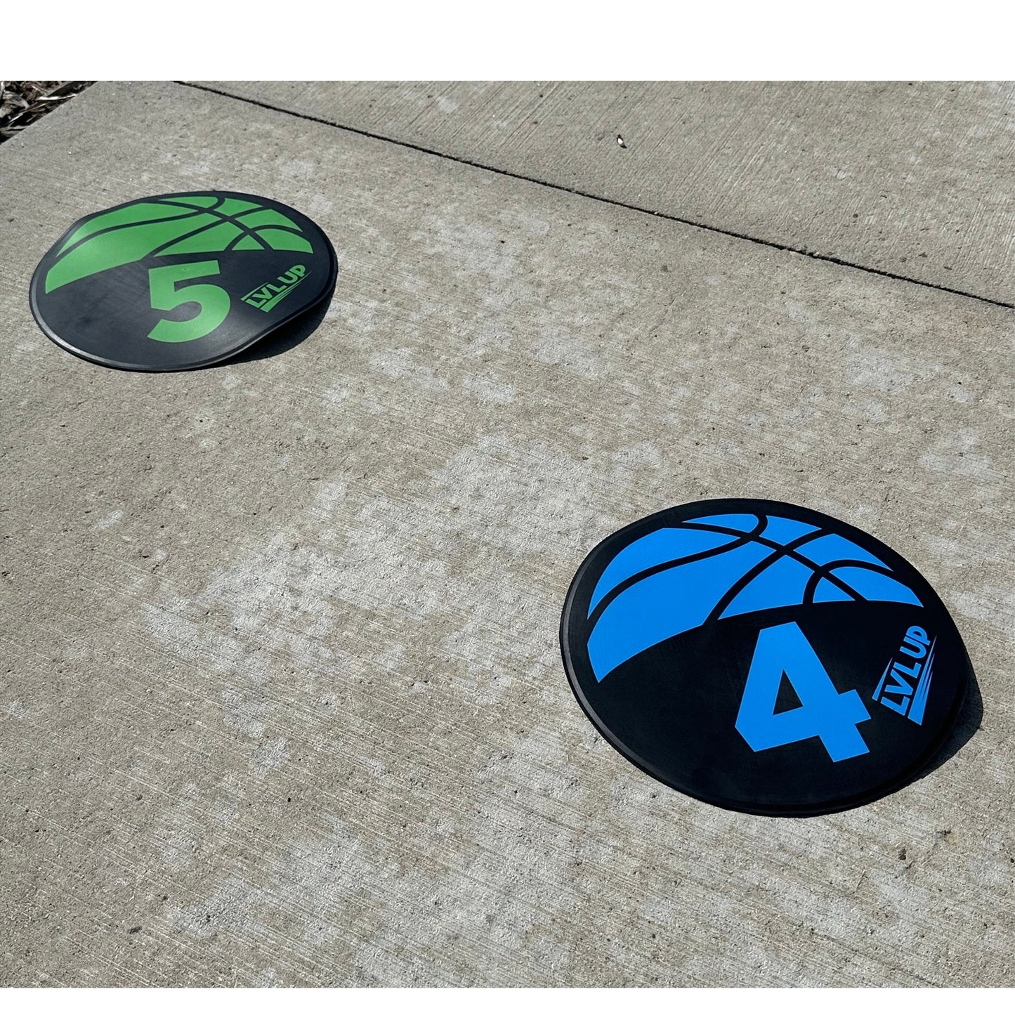 Two black and colored basketball training pads with numbers on concrete.