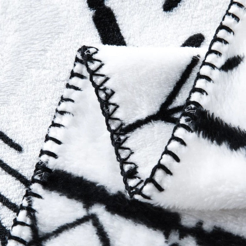 Close-up of a folded white fleece blanket with a black geometric pattern and black stitching along the edges.