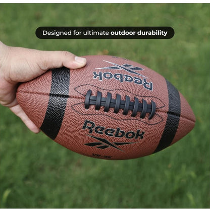 Close-up of a brown Reebok football held by a hand, with the text "Designed for ultimate outdoor durability" in the background.