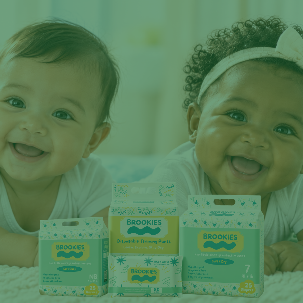 Two smiling babies lying on their stomachs behind a row of Brooke's disposable training pants boxes, with a green-tinted overlay across the photo.
