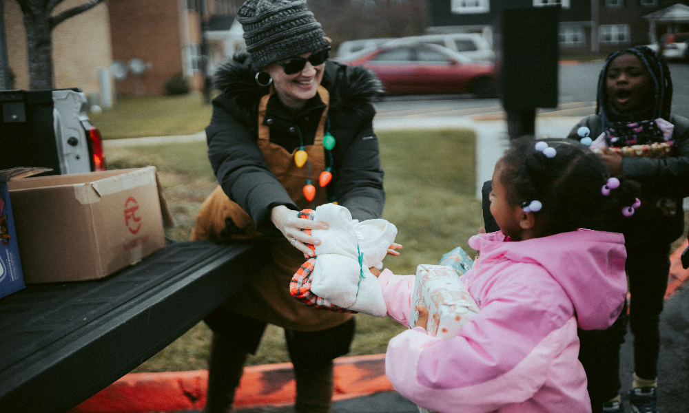 Person handing out candy to children from a truck bed on a cold day.