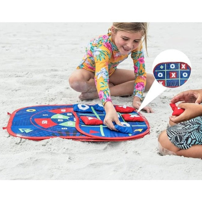 Young girl playing a bean bag toss game on a beach, with a "tic-tac-toe" arrangement.
