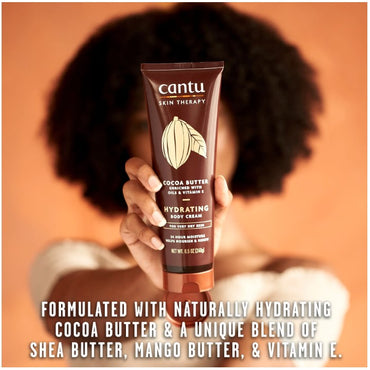 A woman holds up a brown tube of Cantu cocoa butter hydrating body cream.