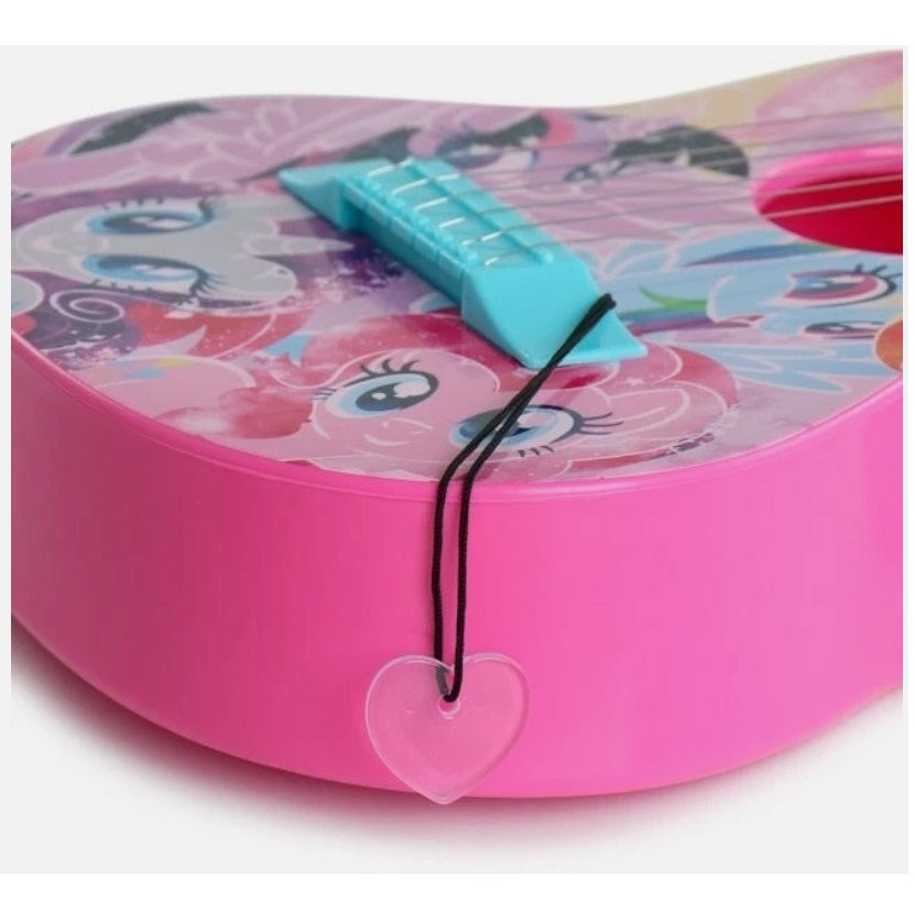 Close-up of a pink My Little Pony toy guitar with a transparent heart charm hanging from a black cord.
