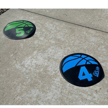 Two black and colored basketball training pads with numbers on concrete.