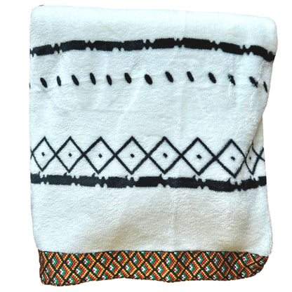 White fuzzy blanket with black patterns and a colorful, patterned border.
