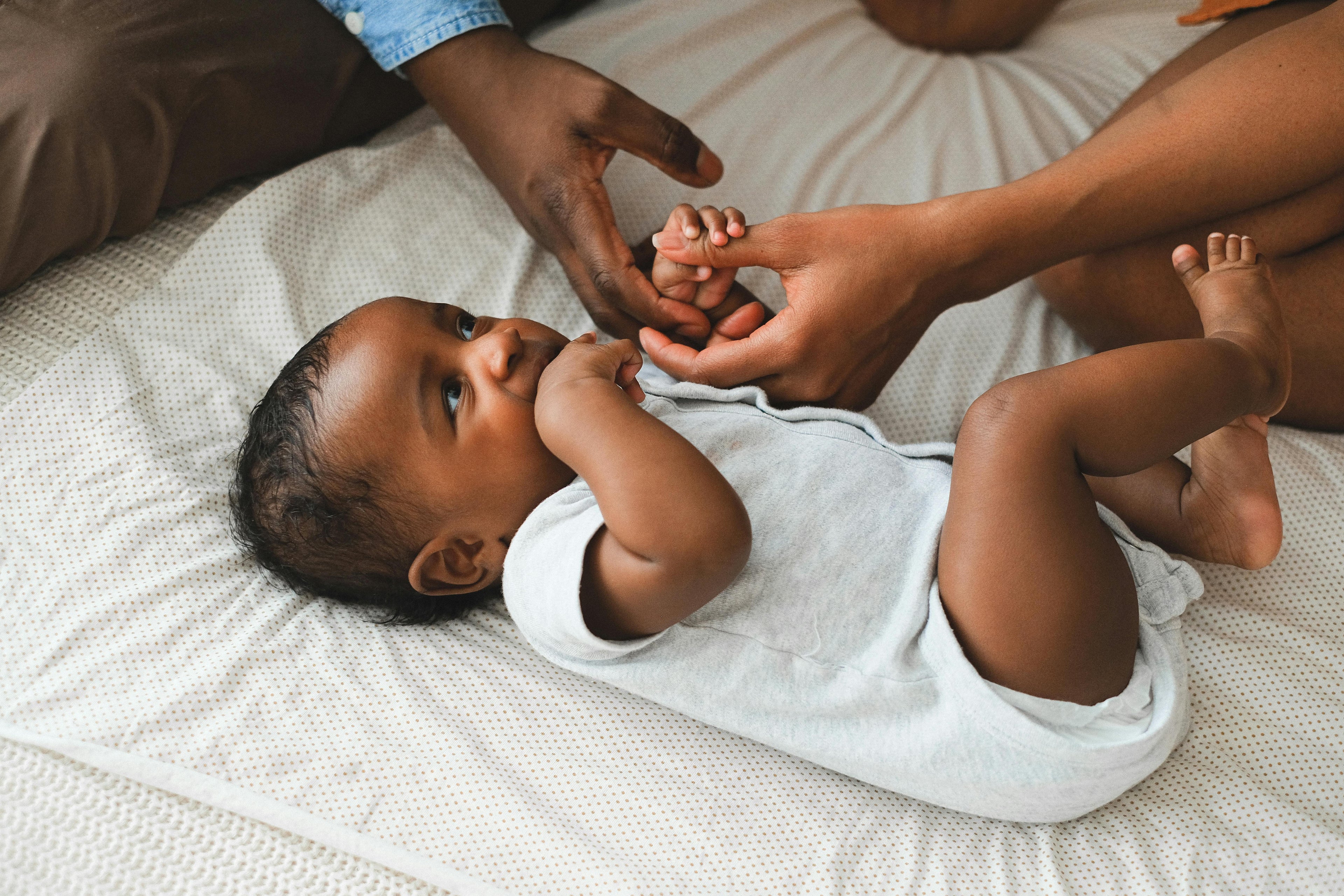 Baby lying on a bed with an adult's hand touching its feet
